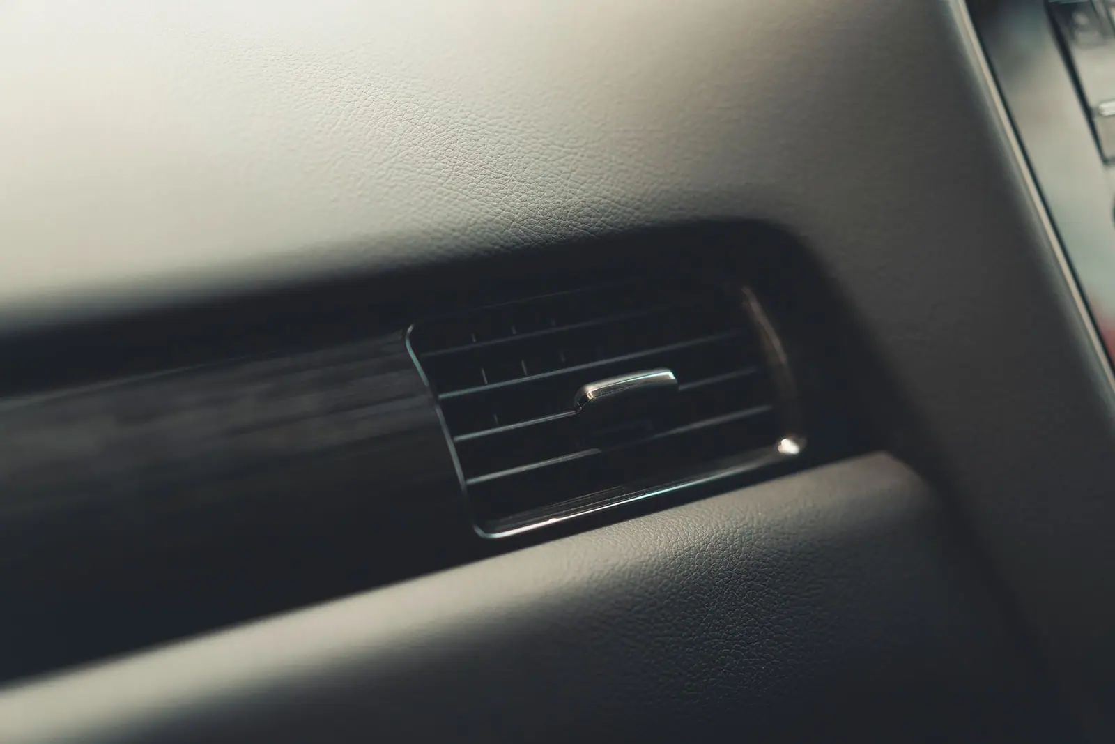 A rectangular air vent and trim on a car's passenger-side dashboard