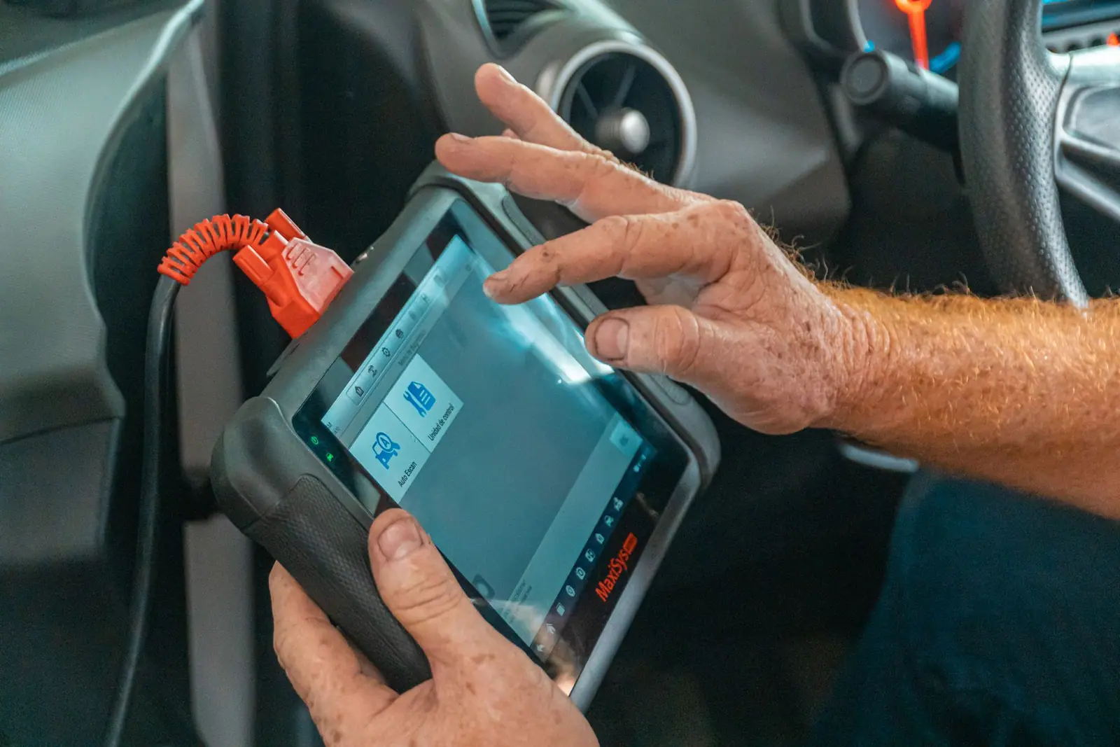 A person holding a blue diagnostic tool inside a car