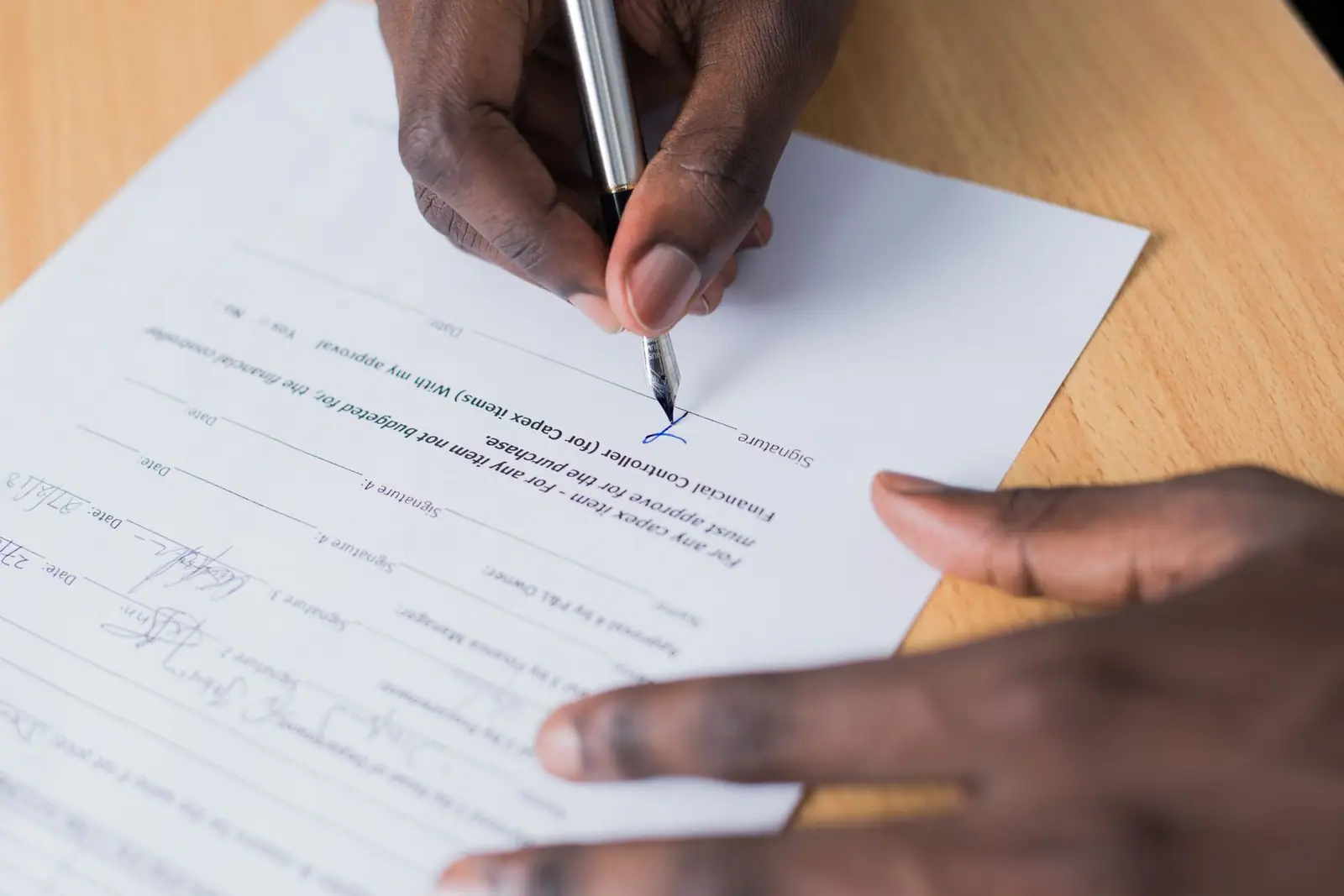 A hand signing a printed document with a pen on a wooden table