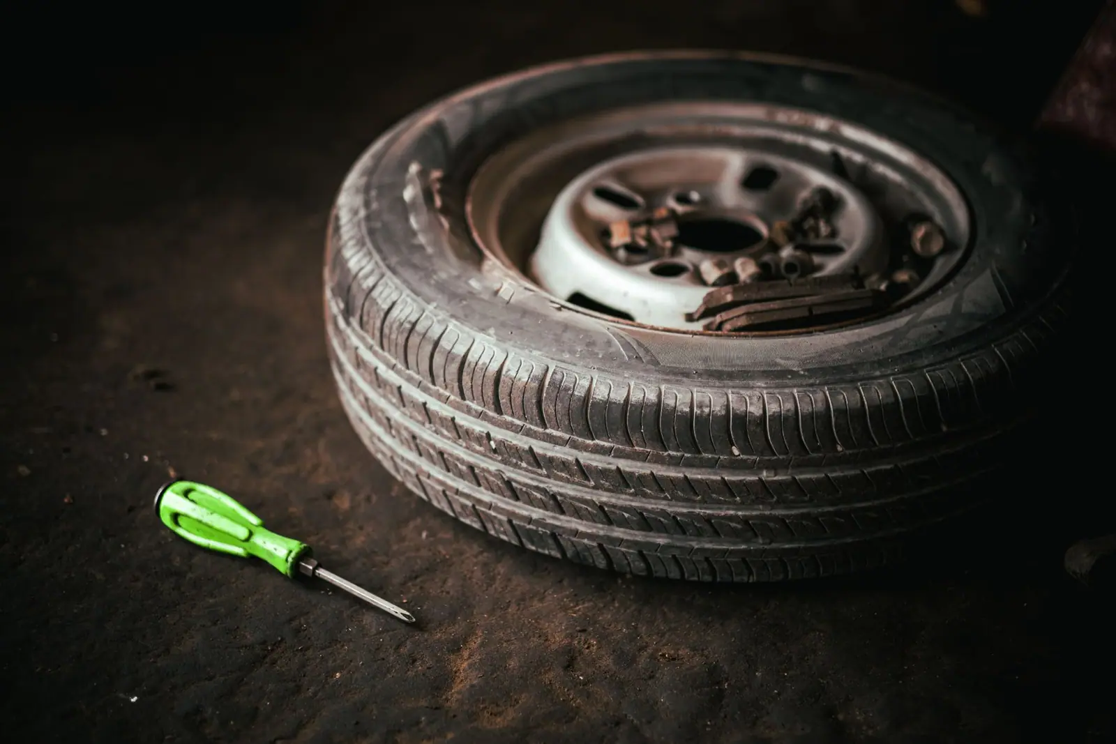A removed wheel and tire on a workshop floor beside a green-handled screwdriver