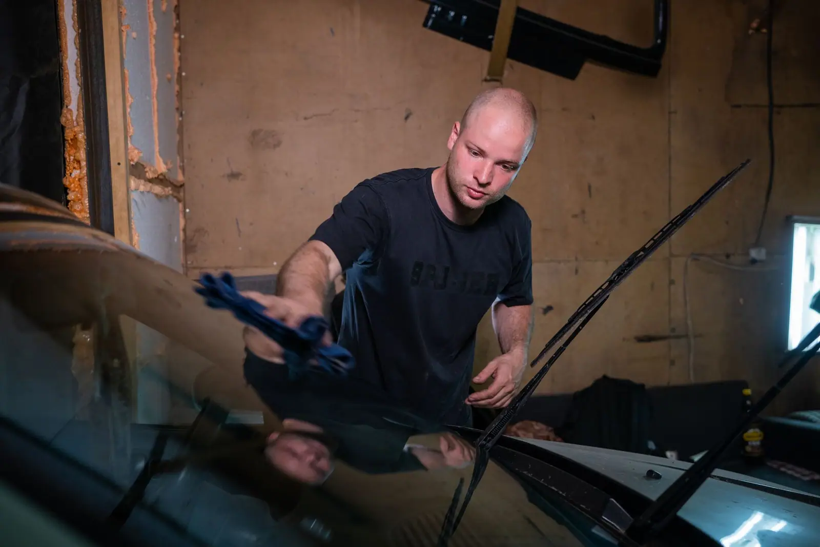 A man wiping a car's front windshield in a workshop